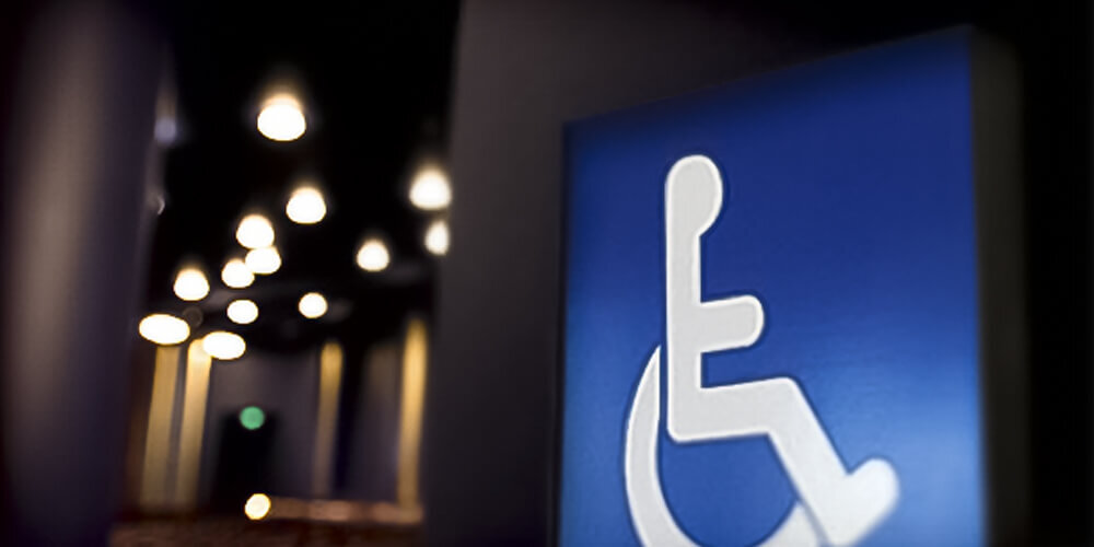 Wheelchair symbol hanging on a dimly lit wall with Hobby Center ceiling lights in the background