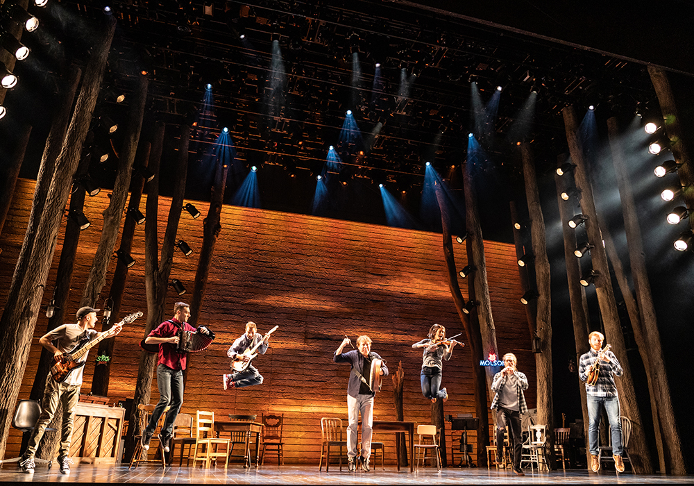 Musical performance on a stage with a wooden backdrop and trees